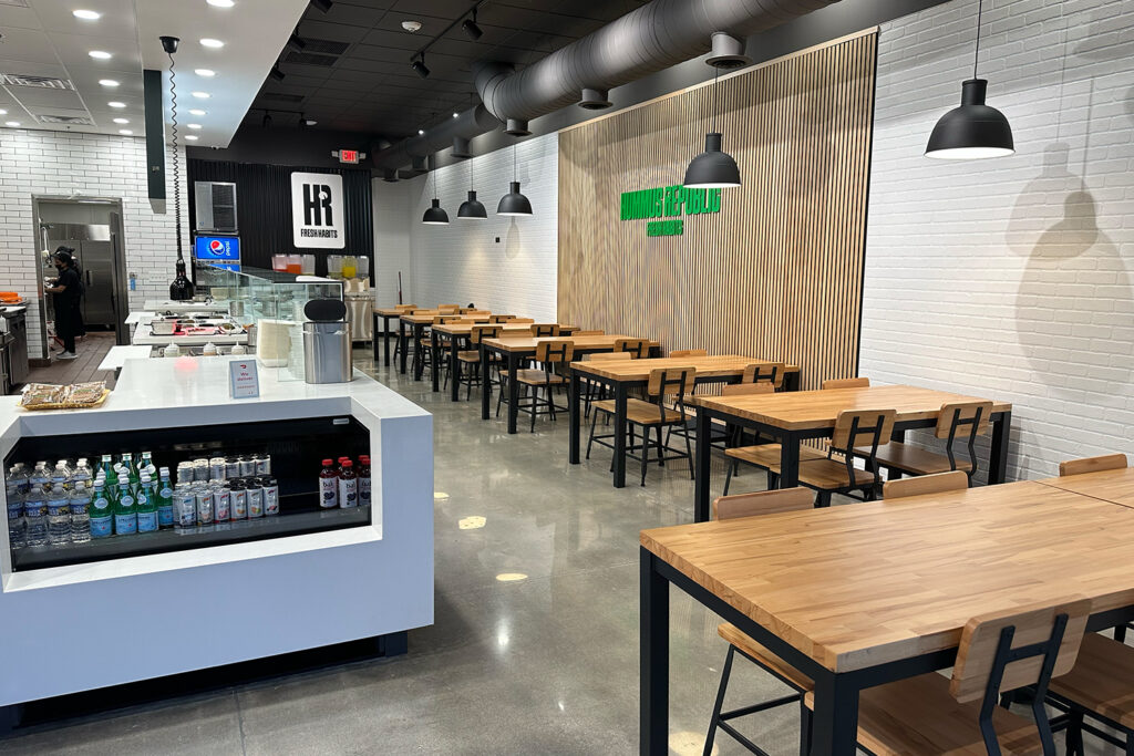 The Questions You Should Be Asking a Franchisor at Discovery Day — and Why Most People Don't modern fast casual restaurant interior with wooden tables, black chairs, a counter displaying drinks and food, and a staff member working in the background.