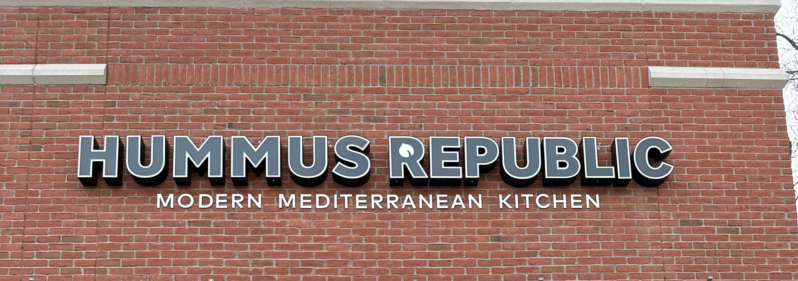 When Is the Right Time to Hire a General Manager — and What Changes When You Do A couple co-owning a husband and wife co owned franchise standing proudly behind the counter of their Mediterranean fast-casual restaurant