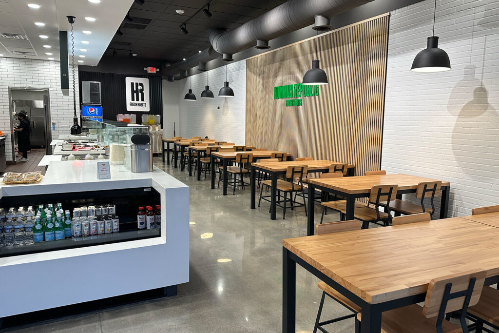 modern restaurant interior with wooden tables and black chairs, beverage display, and a counter area; wall sign reads handel’s homemade ice cream.