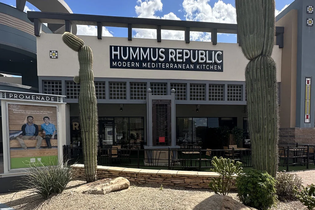 outdoor view of hummus republic restaurant with patio seating, large cacti, and a sign reading modern mediterranean kitchen on the building facade. outdoor view of hummus republic restaurant with patio seating, large cacti, and a sign reading modern mediterranean kitchen on the building facade.