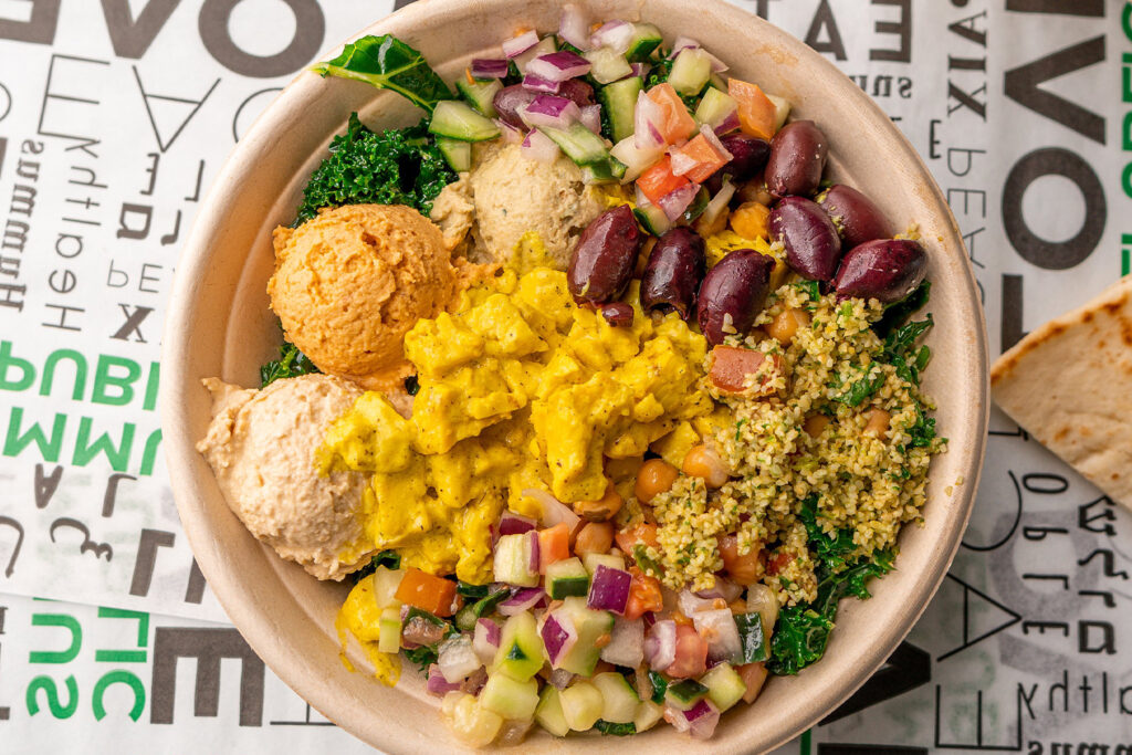 Why the Best Marketing for a Mediterranean Restaurant Is Already in Your Neighborhood a bowl with kale, hummus, falafel, tabbouleh, diced cucumbers, tomatoes, red onion, kalamata olives, and a yellow sauce, with pita bread on the side.
