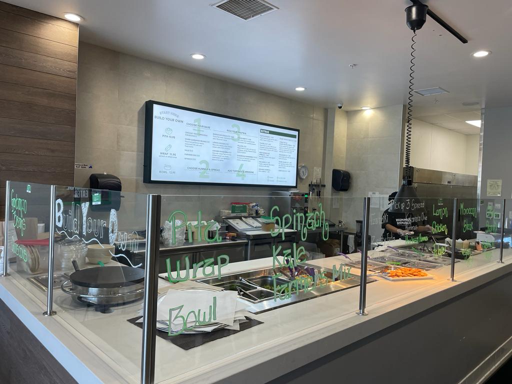 No, Owning a Franchise Is Not Just Buying Yourself a Job — Here's the Difference a modern cafeteria counter with a glass barrier, salad ingredients, and a menu displayed on a digital screen in the background.