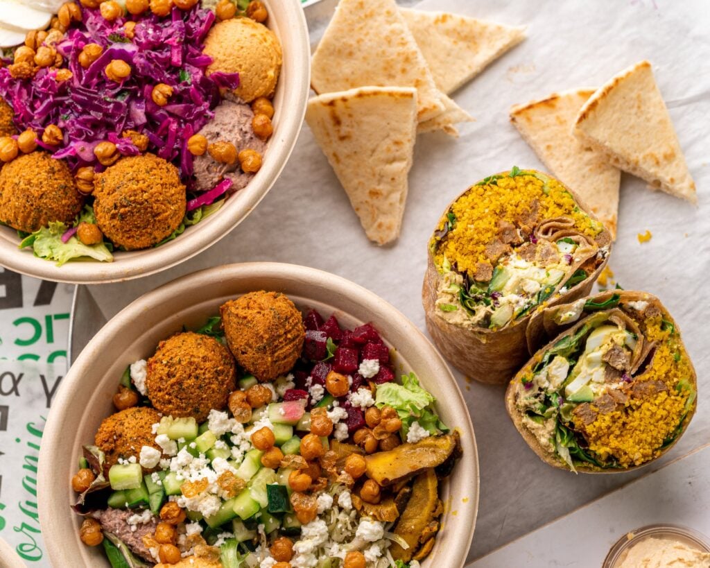 Why Owning a Business That Reflects Your Culture Changes Everything two bowls with falafel, chickpeas, vegetables, and cheese, a sliced wrap with similar fillings, and pita triangles on a white surface.