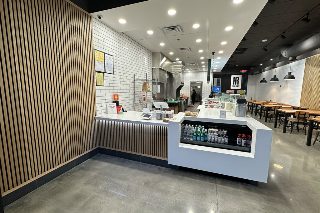Think You Need $500K to Buy a Franchise? Here's What the Numbers Actually Show modern fast casual restaurant interior with a white countertop, beverage display, wooden accents, and seating area with tables and chairs in the background.